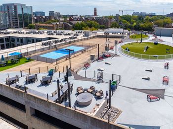 A rooftop with a pool, loungers and a trampoline surrounded by buildings.